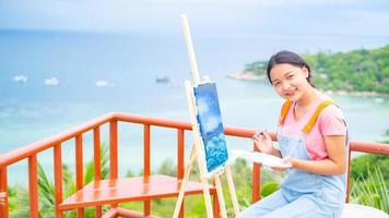 Young girl using brush drawing picture on canvas paper, at beautiful landscape view at koh tao Thailand. photo