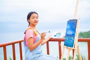 niña usando un dibujo de pincel sobre papel de lienzo, en una hermosa vista del paisaje en koh tao, tailandia.