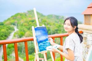 Young girl using brush drawing picture on canvas paper, at beautiful landscape view at koh tao Thailand. photo