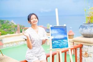 Young girl using brush drawing picture on canvas paper, at beautiful landscape view at koh tao Thailand. photo