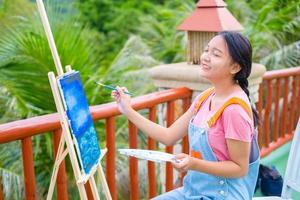 Young girl using brush drawing picture on canvas paper, at beautiful landscape view at koh tao Thailand. photo