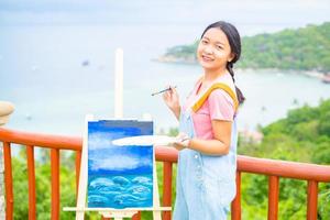 Young girl using brush drawing picture on canvas paper, at beautiful landscape view at koh tao Thailand. photo