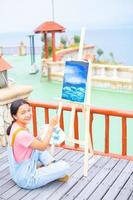 Young girl using brush drawing picture on canvas paper, at beautiful landscape view at koh tao Thailand. photo