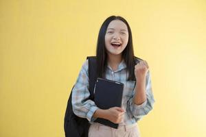 Beautiful young girl with backpack and hold laptop on yellow background. photo