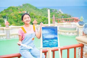 Young girl using brush drawing picture on canvas paper, at beautiful landscape view at koh tao Thailand. photo