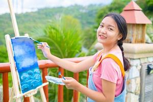 Young girl using brush drawing picture on canvas paper, at beautiful landscape view at koh tao Thailand. photo