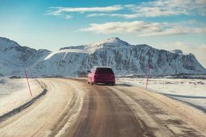 Red SUV car driving on rural road with mountain in winter photo