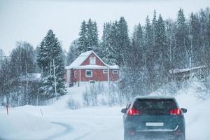 Car driving in blizzard with red house in countryside on winter photo