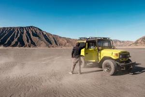 hombre turista de pie en un coche amarillo de cuatro ruedas en el desierto foto