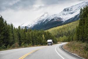 viaje por carretera de una autocaravana conduciendo por una carretera con montañas rocosas en un bosque de pinos en el parque nacional de banff foto