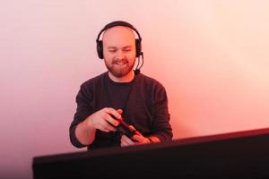 un hombre alegre que usa auriculares está jugando con su joystick en la computadora. foto