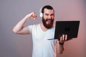 un hombre poderoso y emocionado está haciendo el gesto ganador mientras sostiene una computadora portátil.