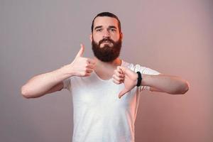 Porrtait of young bearded hipster man showing like and dislike gesture. photo