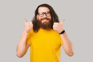 feliz joven barbudo en camiseta amarilla mostrando pulgares arriba gesto y sonriendo foto