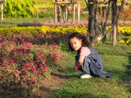 la niña se sienta en la hierba, usando una lupa para mirar las flores en el campo foto