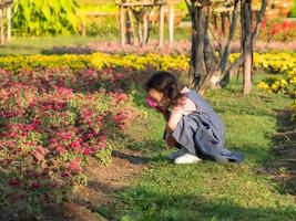 la niña se sienta en la hierba, usando una lupa para mirar las flores en el campo foto