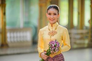 atractiva mujer tailandesa con un antiguo vestido tailandés sostiene flores frescas que rinden homenaje a buda para pedir un deseo en el festival tradicional de songkran en tailandia foto