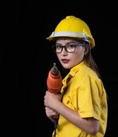 una mujer hermosa con el uniforme técnico amarillo sostiene un taladro usado en la construcción foto