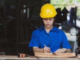 Woman working in mechanic uniform using measuring tools to cut wood sheets in factory photo