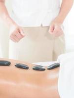 An expert masseuse at a spa salon puts hot stone on the back of an Asian woman to relieve tension from work photo