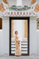 A graceful Thai woman in Thai dress adorned with precious jewelry holds a flower garland through the beautiful ancient Thai temple gates photo