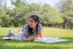 una chica medio tailandesa se relaja en el parque y escribe un lápiz en un lienzo pintado foto