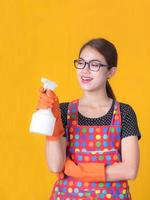hermosa mujer asiática sosteniendo una botella de spray para limpiar el dispositivo y sonriendo alegremente para limpiar la casa foto