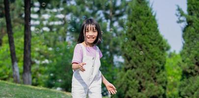 Image of Asian little girl playing with soap bubbles at park photo