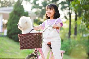 Image of Asian little girl cycling with her pet dog at the park