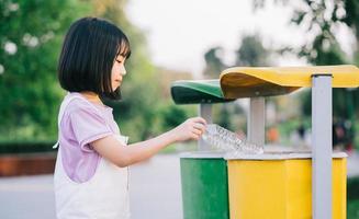 Image of Asian little girl puts used plastic bottles in the trash photo
