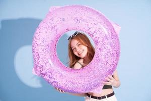 Image of young Asian girl holding swimming float on blue background, summer vacation concept photo