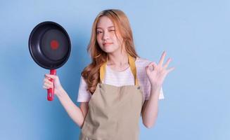 Image of young Asian woman holding pan on blue background photo