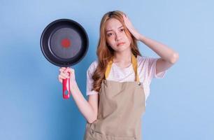 Image of young Asian woman holding pan on blue background photo