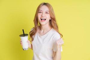 Image of young Asian girl drinking milk tea on yellow background photo