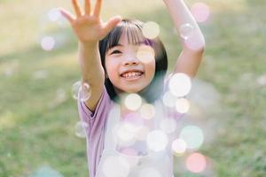 Image of Asian little girl playing with soap bubbles at park photo
