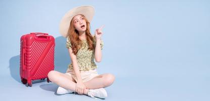 Full length image of young Asian girl with suitcase on blue background, travel concept photo