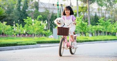 imagen de una niña asiática en bicicleta con su perro mascota en el parque foto