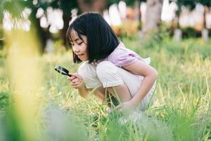 Asian little girl is using magnifying glass to play in the park photo