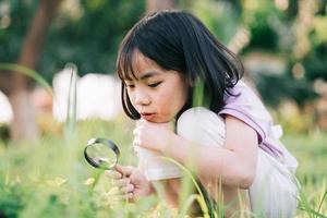 Asian little girl is using magnifying glass to play in the park photo