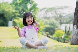 Image of Asian little girl playing with soap bubbles at park photo