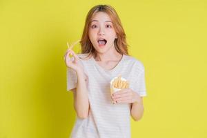 Image of young Asian girl eating french fries on yellow background photo