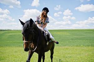 jovencita bonita montando un caballo en un campo en un día soleado. foto