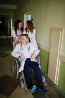 jóvenes médicos locos divirtiéndose posando en una silla de ruedas en el pasillo del hospital.