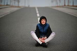 Boy in hoodie sitting at center of road. photo