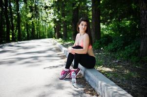 Fitness sport girl in sportswear sitting at road in park with water at bottle, outdoor sports, urban style. photo