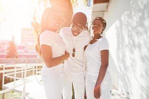 tres elegantes y alegres amigos afroamericanos, vestidos con ropa blanca. moda callejera de jóvenes negros. hombre negro con dos africanos bajo el sol. foto