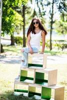 retrato de una chica vestida a la moda posando en cajas de madera en el parque en un día soleado foto