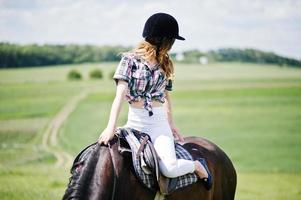 jovencita bonita montando un caballo en un campo en un día soleado. foto