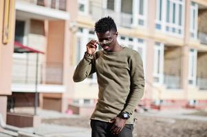 Handsome and attractive african american man in sunglasses posing next to the tall building on a street. photo