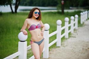 retrato de una bella modelo posando contra la valla con gafas de sol en la orilla del lago. foto